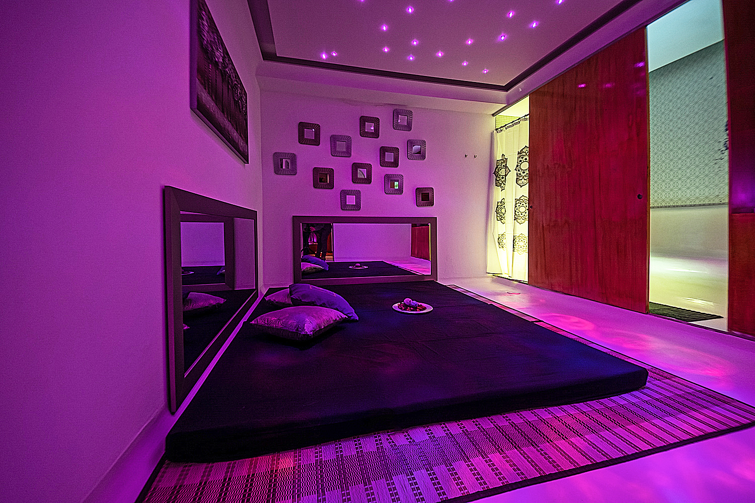 Sala de massagens com iluminação roxa, tatami e almofadas.